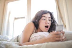 An image of a shocked woman after looking at a man's penis on her phone illustrates the benefits you enjoy after you make your penis grow.