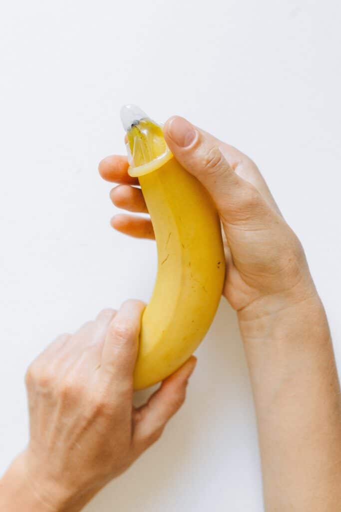 Hand skillfully demonstrating a condom application on a ripe yellow banana, representing natural lifetime penis enlargement